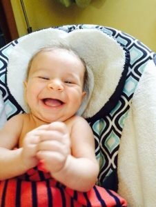 A baby laughing in a car seat Description automatically generated